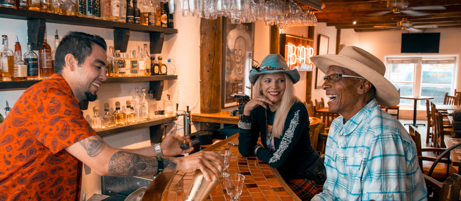 Laughing friends are served a drink by the bartender in the Adobe Bar