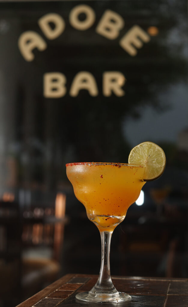 Colorful margarita glass on tile bar with Adobe Bar sign on window in background