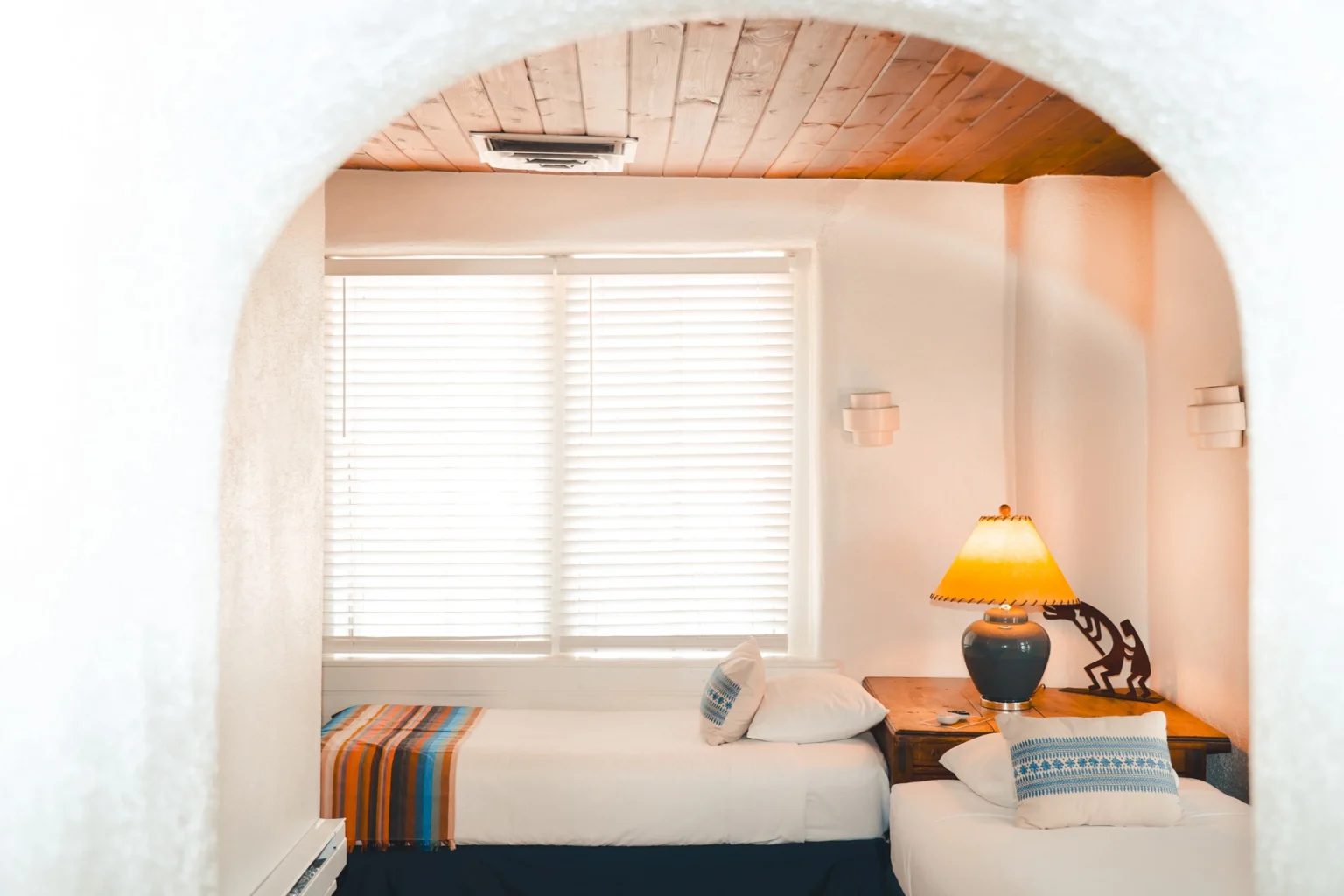 Two twin beds through archway in room corner with lamp