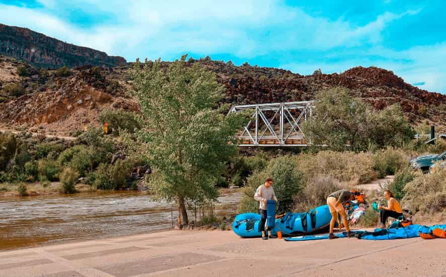 Rafters prepare boats at river's edge near bridge